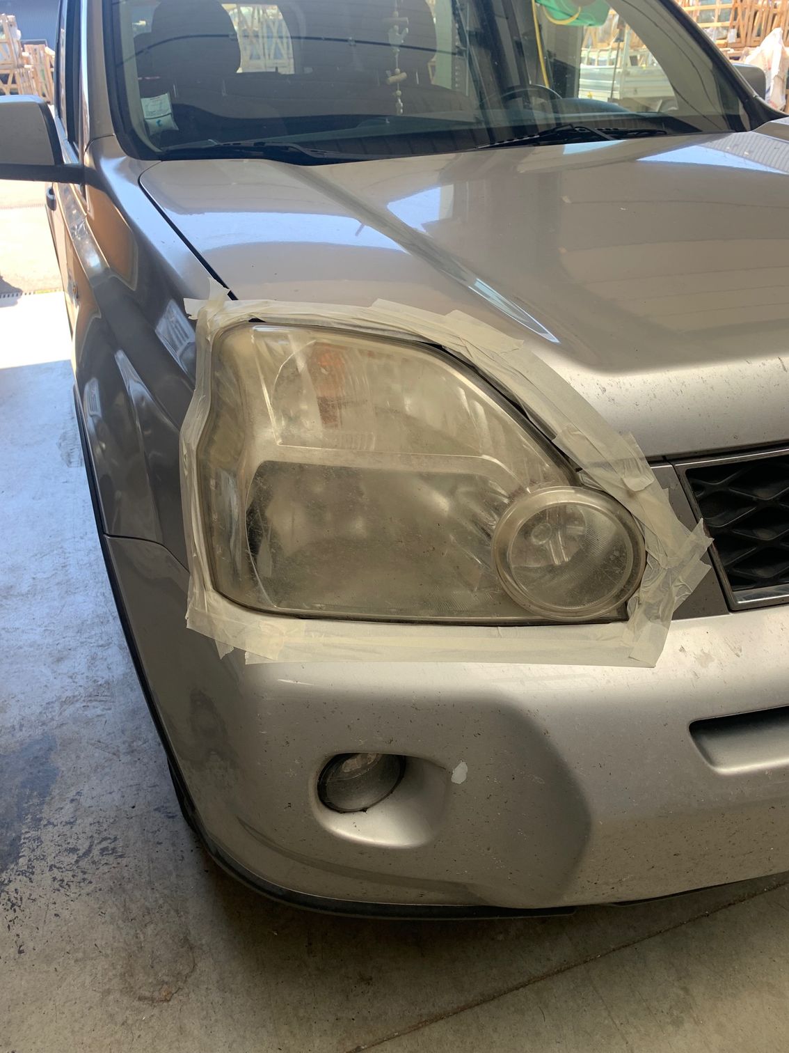 Voiture argentée avec phare avant gauche et pare-chocs endommagés dans un garage.