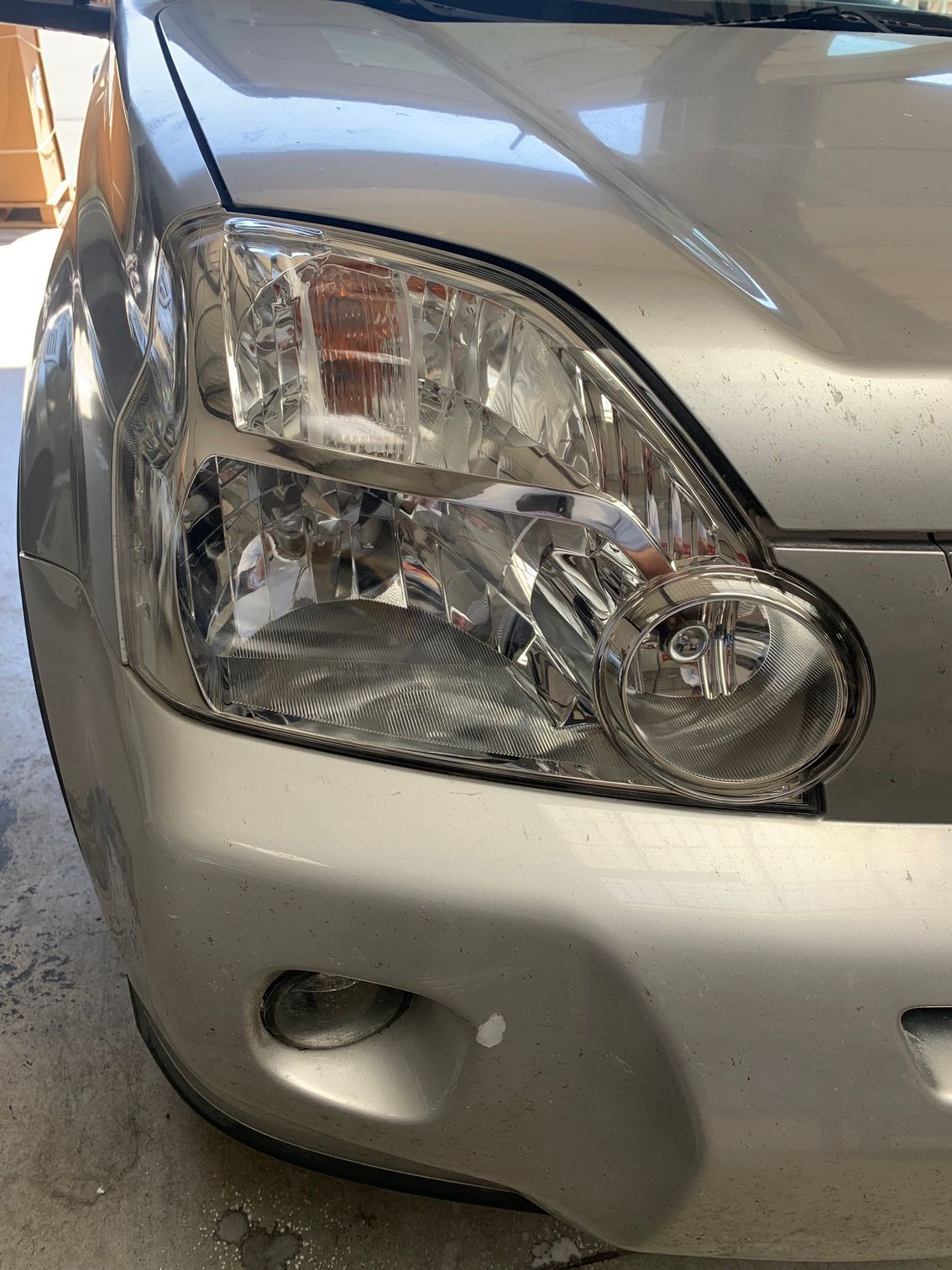 Gros plan sur le phare avant gauche et le pare-chocs endommagés d'une voiture argentée.