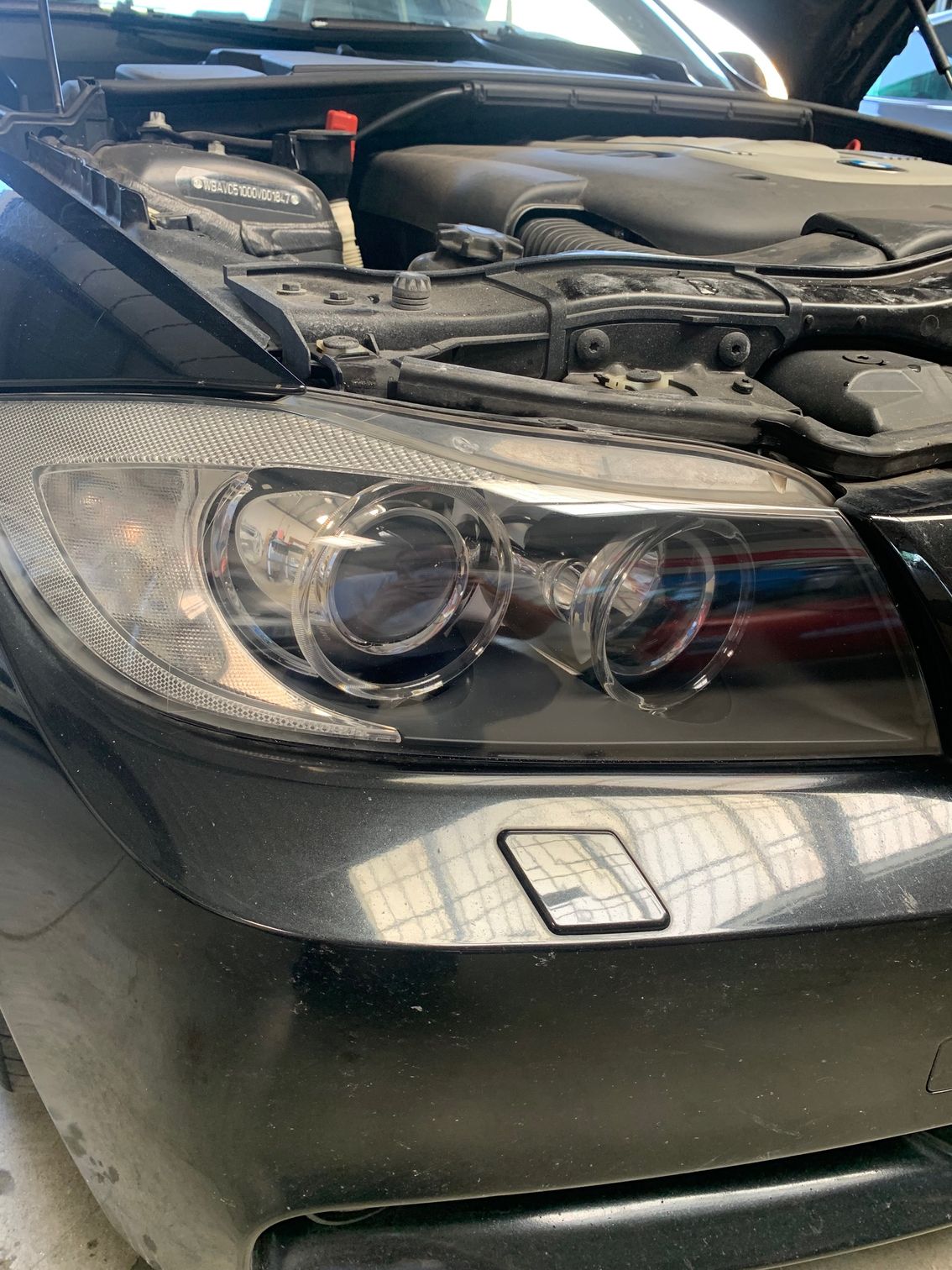Gros plan sur le phare avant et le pare-chocs d'une voiture noire, capot ouvert.