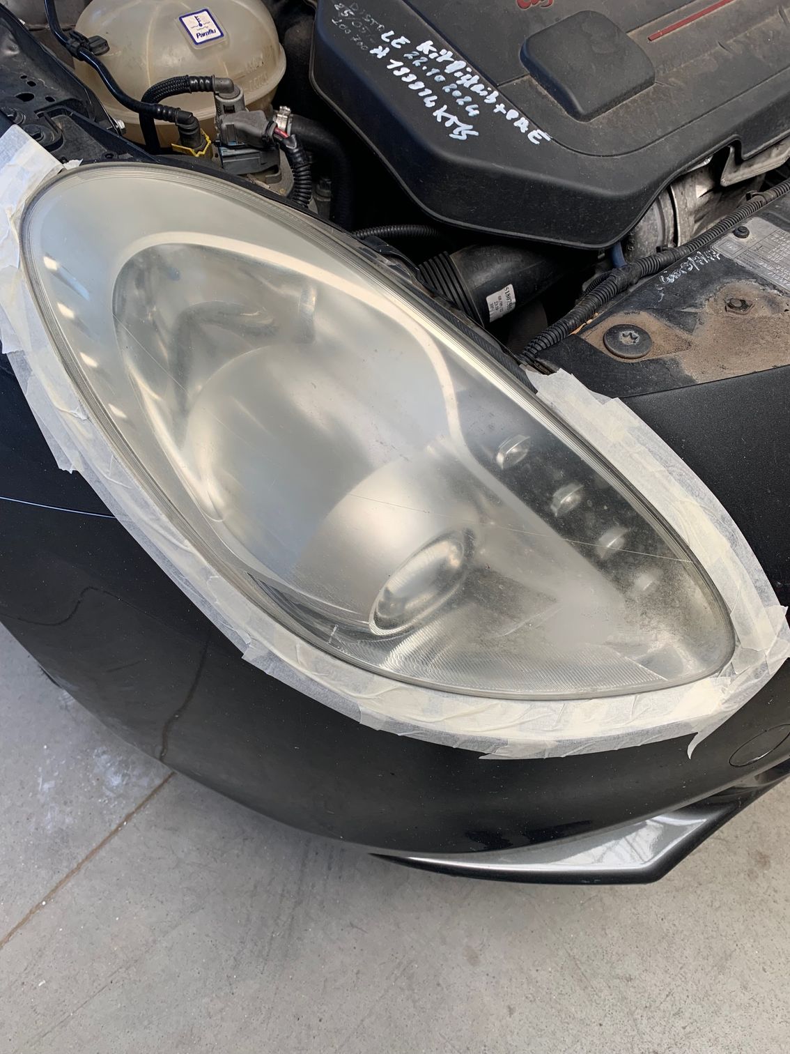 Gros plan sur un phare de voiture opaque et usé, capot ouvert.
