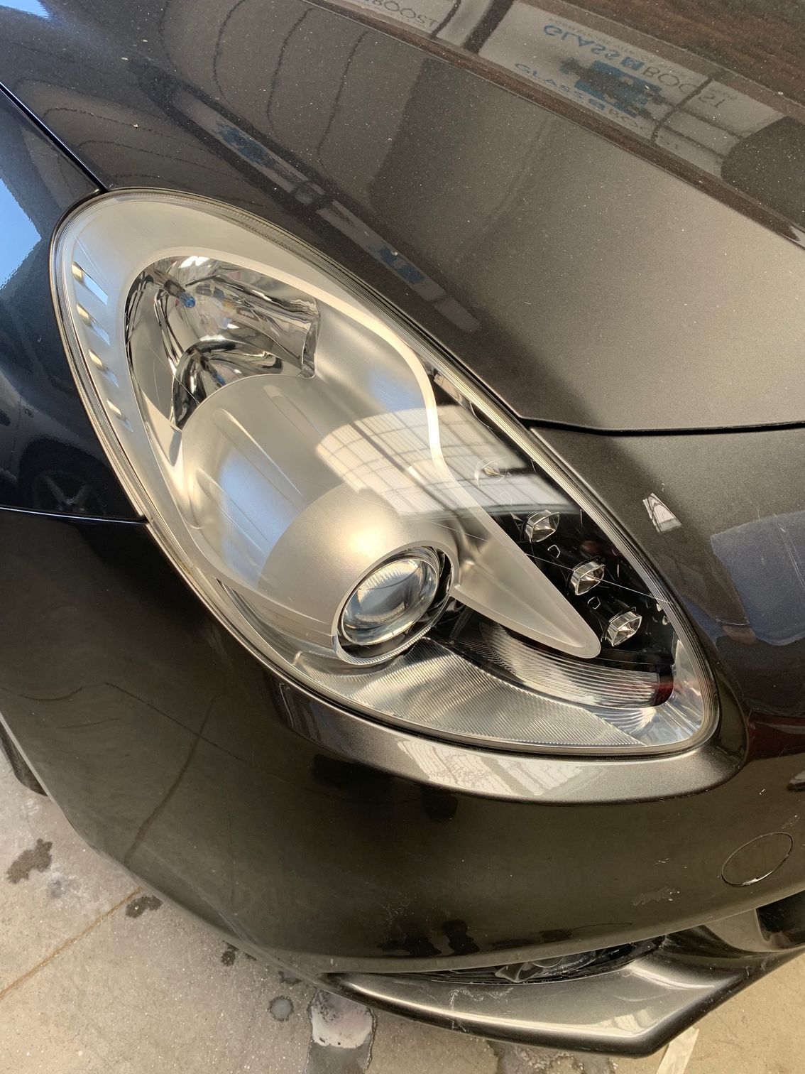 Gros plan sur le phare et le pare-chocs avant d'une voiture gris foncé dans un parking.
