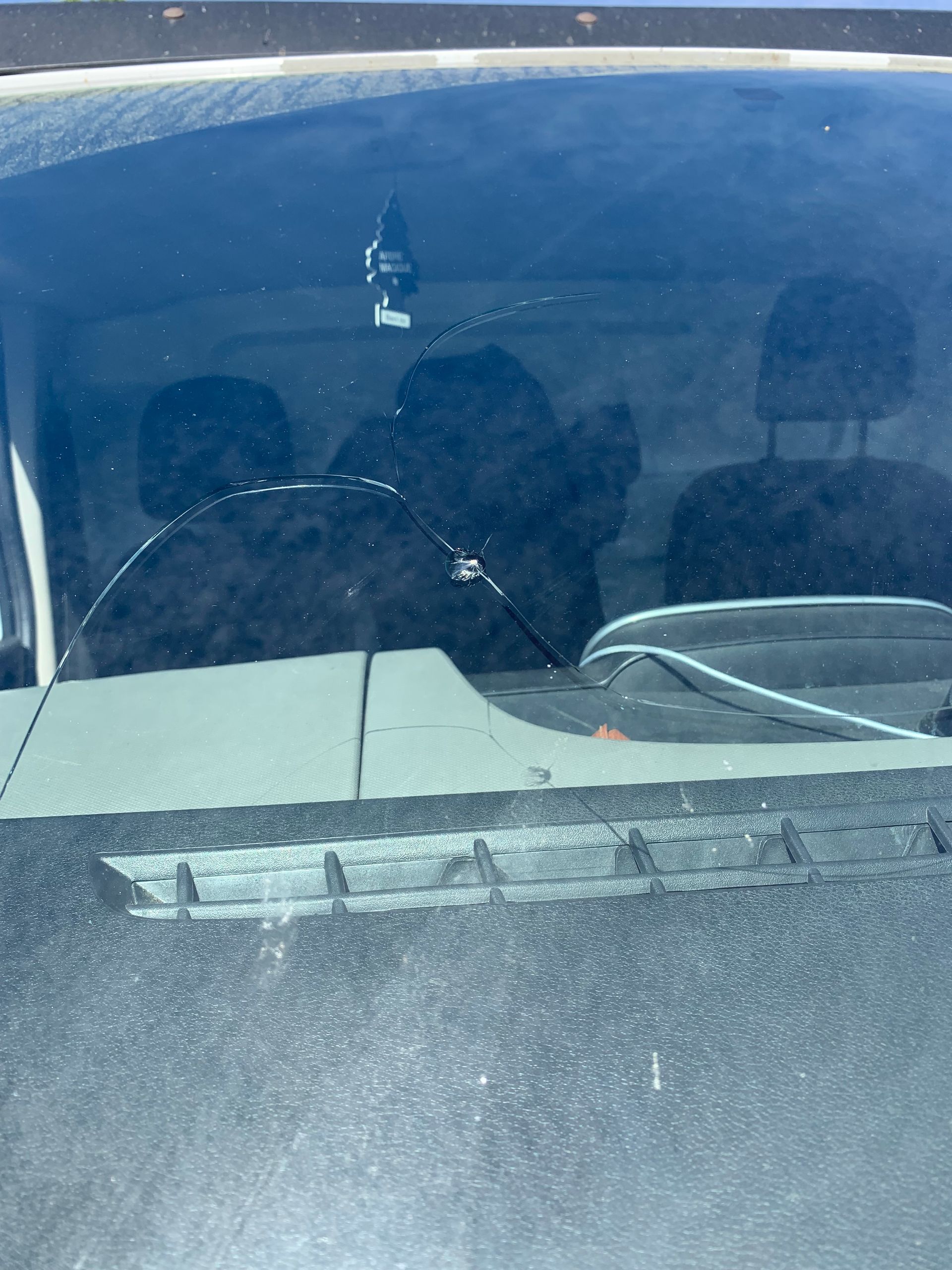 Pare-brise poussiéreux d'une voiture, l'essuie-glace en bas et un objet décoratif suspendu à l'intérieur.