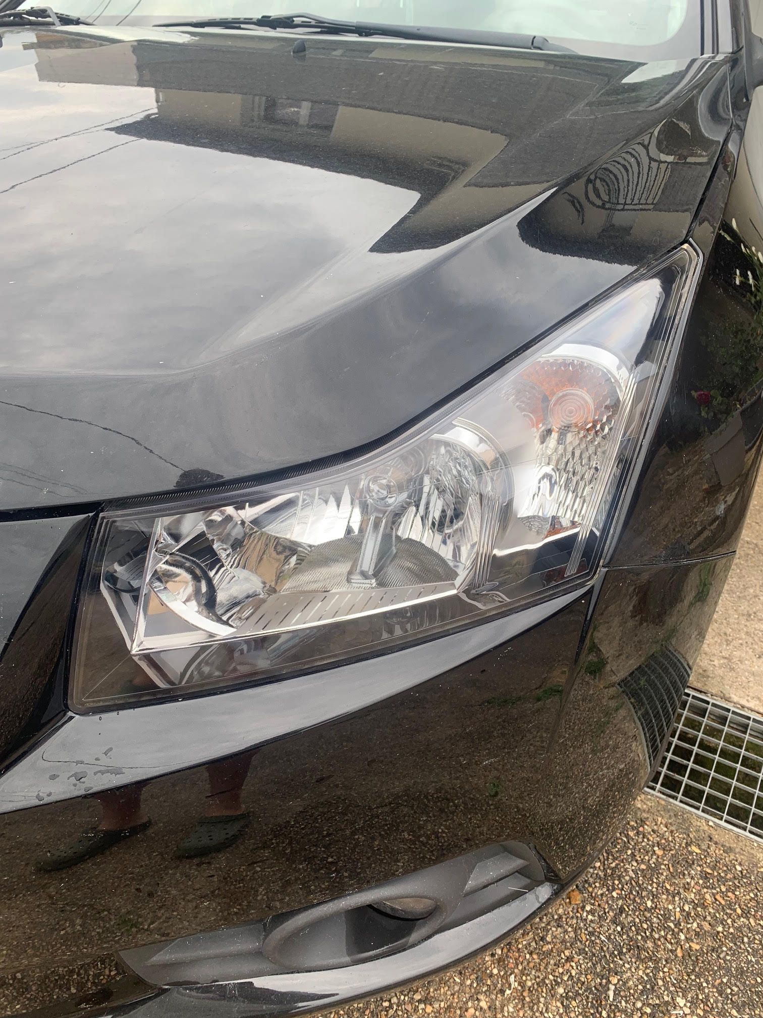Gros plan sur le coin avant d'une voiture noire, montrant le phare, le pare-chocs et la calandre près d'un trottoir.