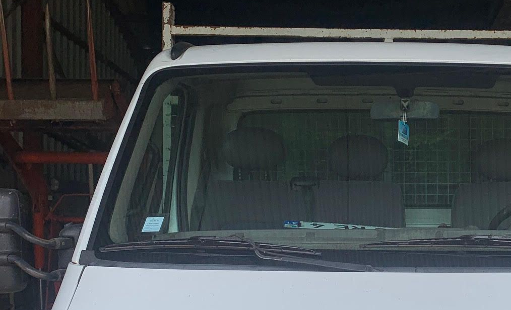 Vue de face du pare-brise d'une camionnette blanche à l'intérieur d'un garage, avec des étagères visibles sur la gauche.