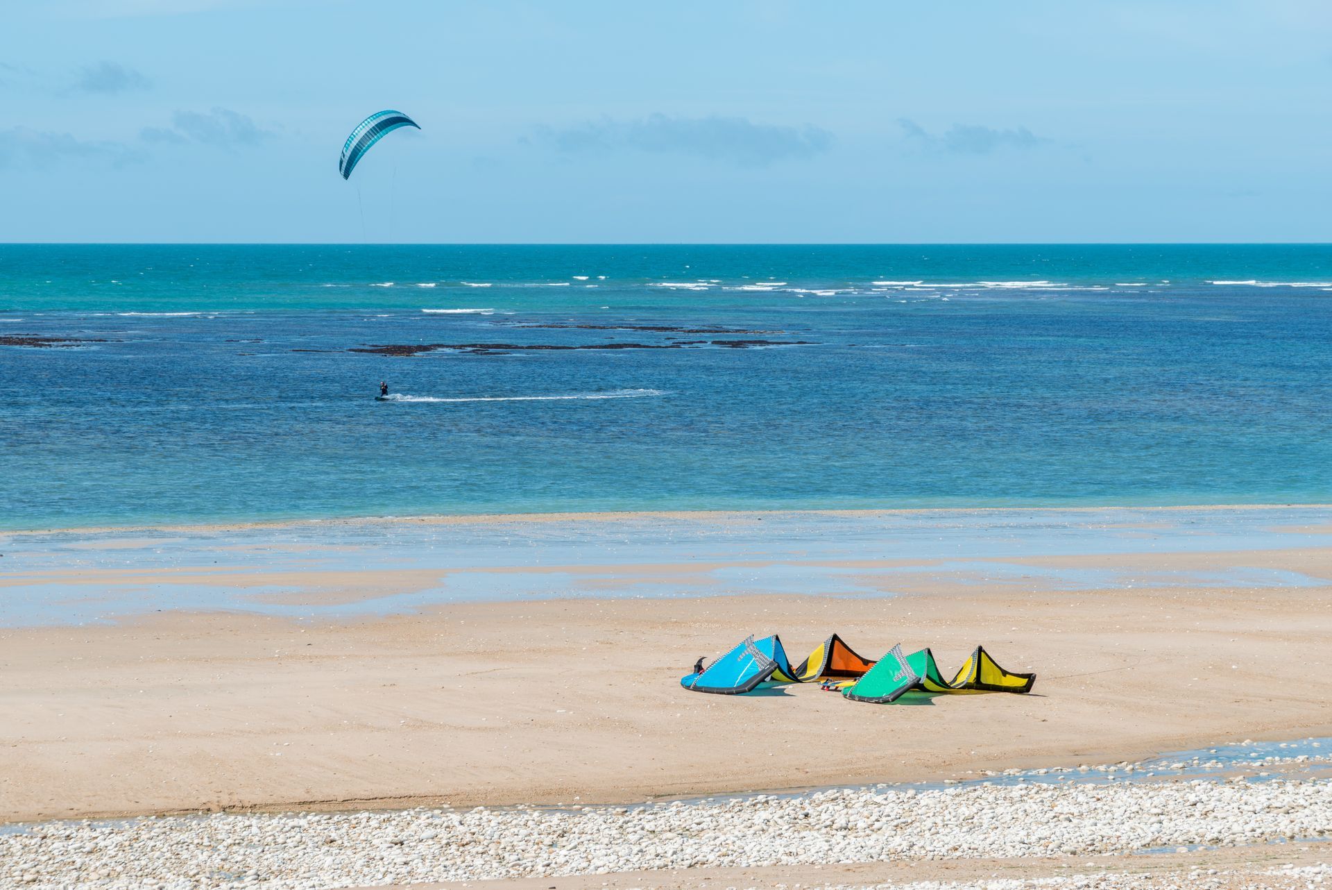 Plusieurs kitesurfs posés sur une plage.