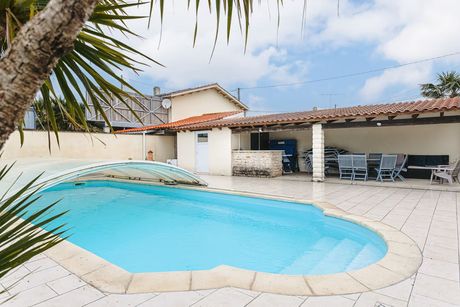 Une piscine devant une maison avec une terrasse couverte.