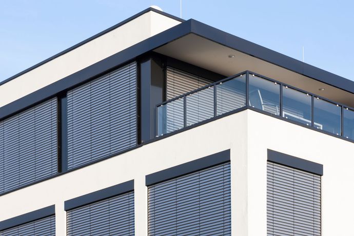 Immeuble moderne blanc avec volets bleus et balcon à balustrade de verre se détachant sur le ciel