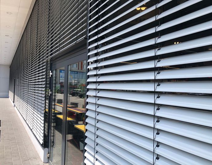 Façade moderne du bâtiment avec persiennes noires, porte vitrée et allée couverte