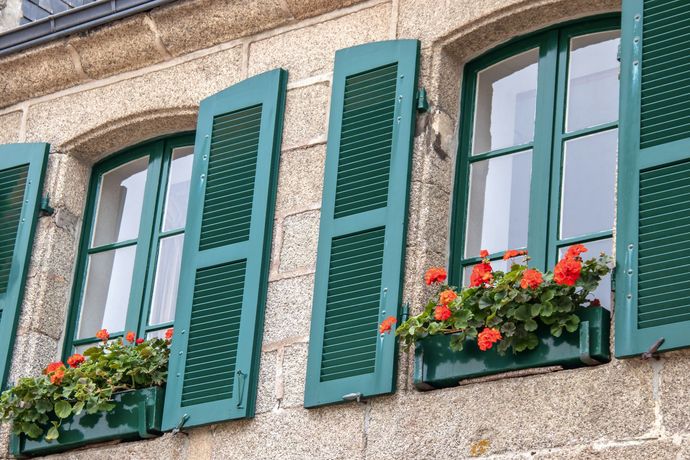 Façade d’un bâtiment avec des volets verts et des jardinières sous des fenêtres en arc