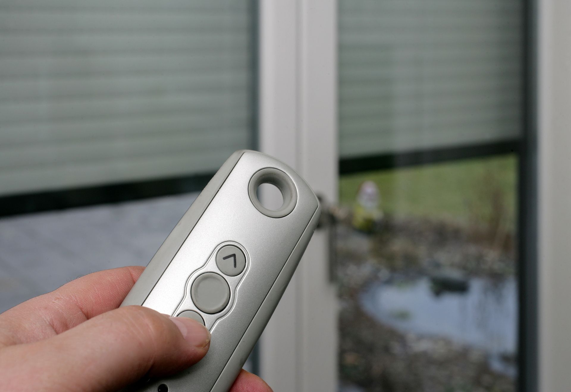 Main tenant une télécommande argentée devant une fenêtre