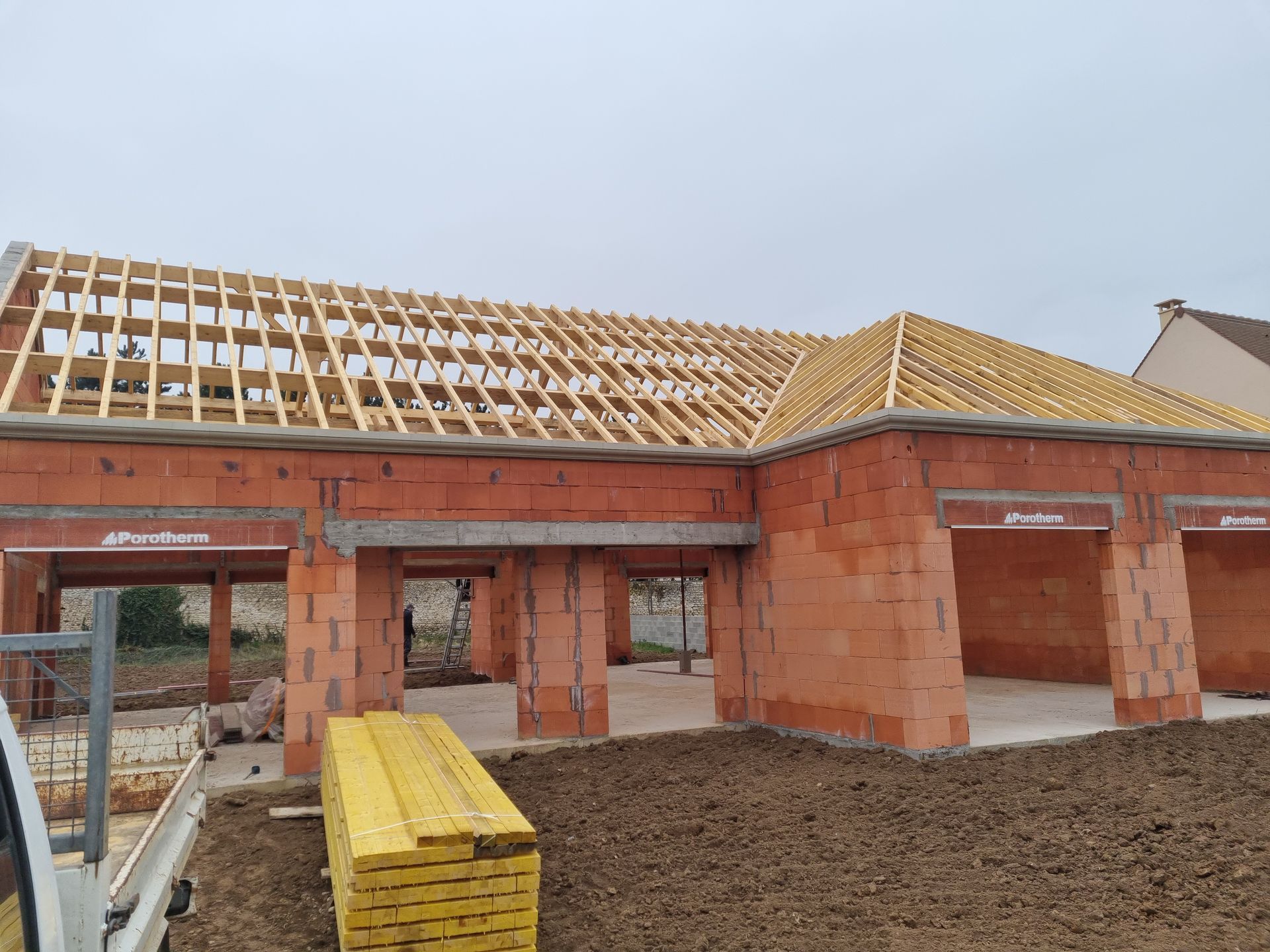 Chantier de construction : structure en briques avec charpente de toit en bois ; temps couvert.