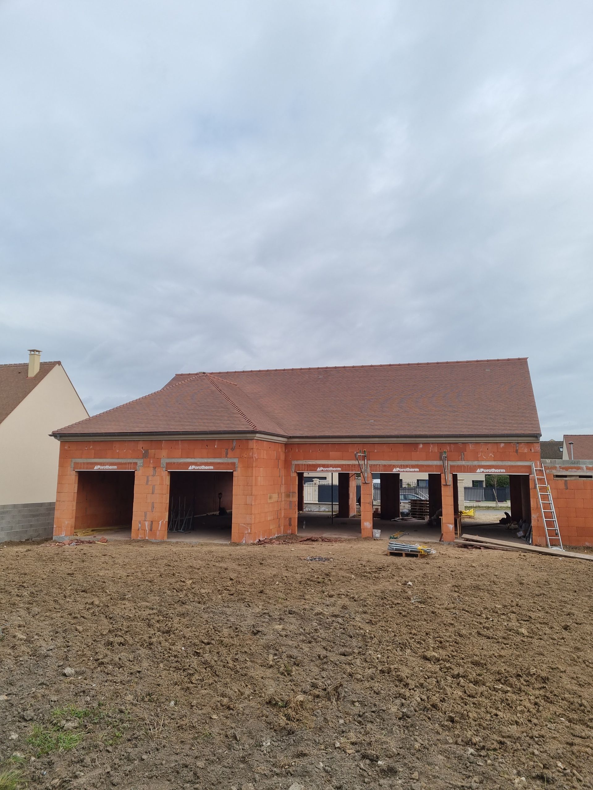Toiture en construction, charpente en bois visible. Ouvriers sur une échelle. Ciel nuageux.