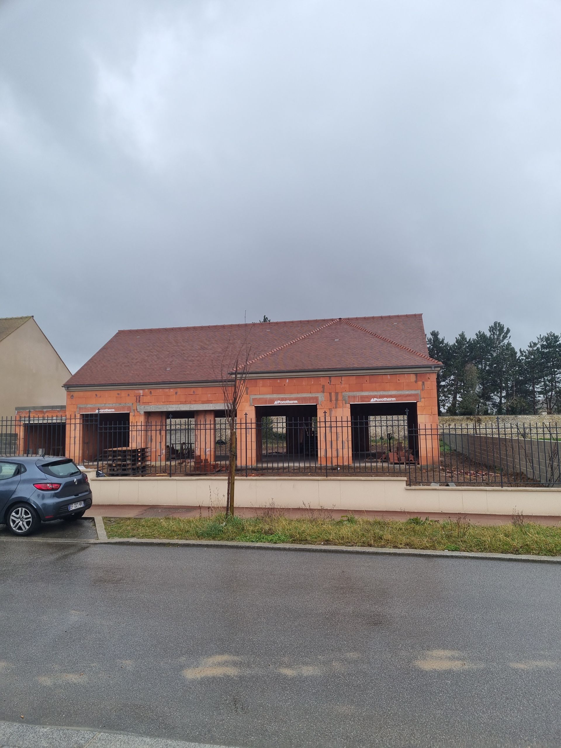 Extérieur d'un bâtiment en briques endommagé, fenêtres calcinées, voiture garée devant, ciel couvert.