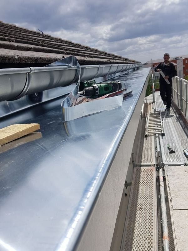 Un couvreur travaille à la pose de solins et de gouttières sur un nouveau toit en métal. Ciel nuageux en arrière-plan.