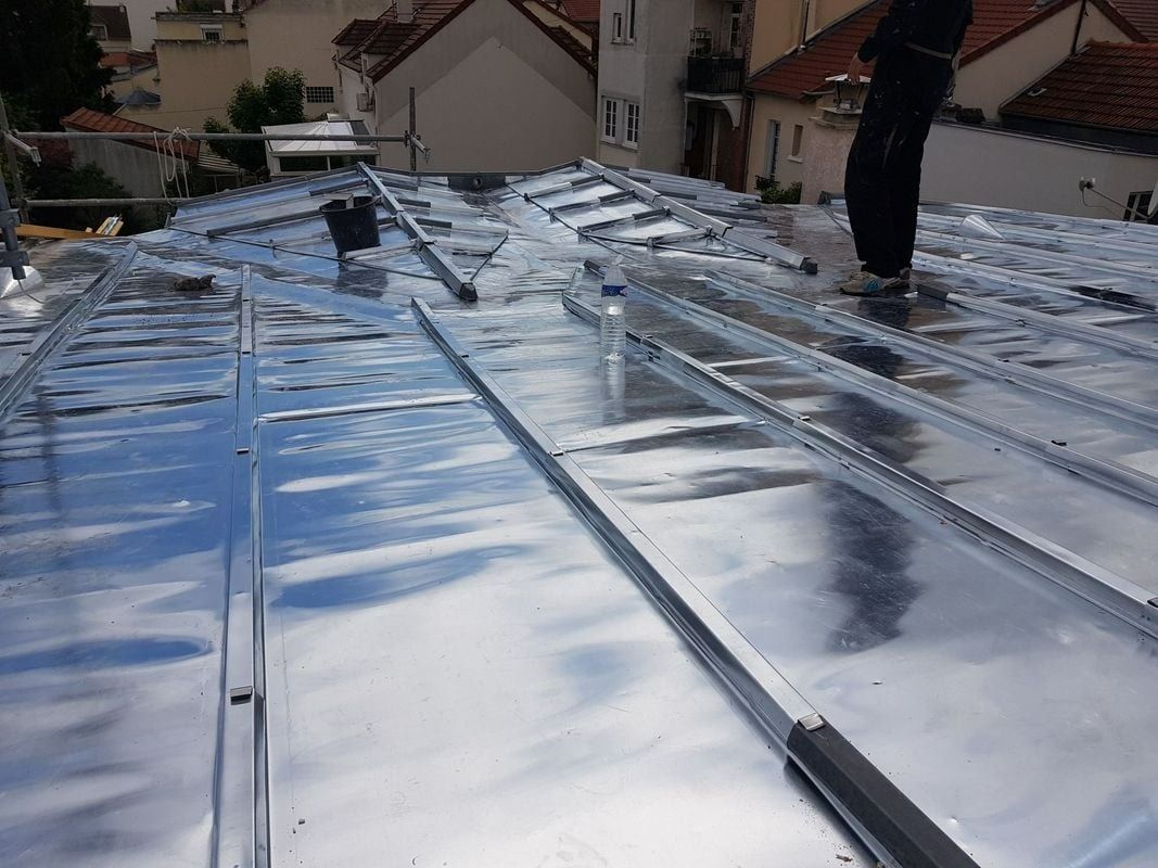 Installation d'une toiture métallique avec une personne debout, toits en arrière-plan.