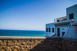Casa blanca junto al mar con vistas a un océano azul bajo un cielo despejado.