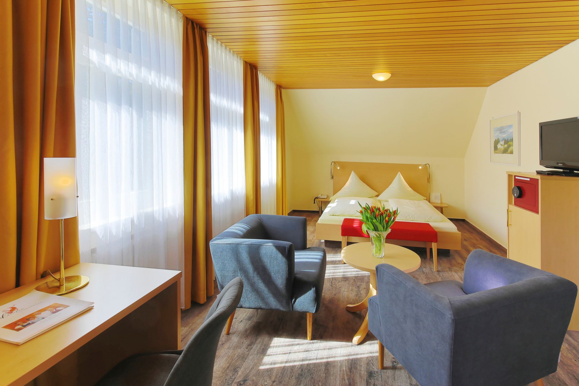 Ein Hotelzimmer mit Bett, Stühlen, Schreibtisch und Fernseher