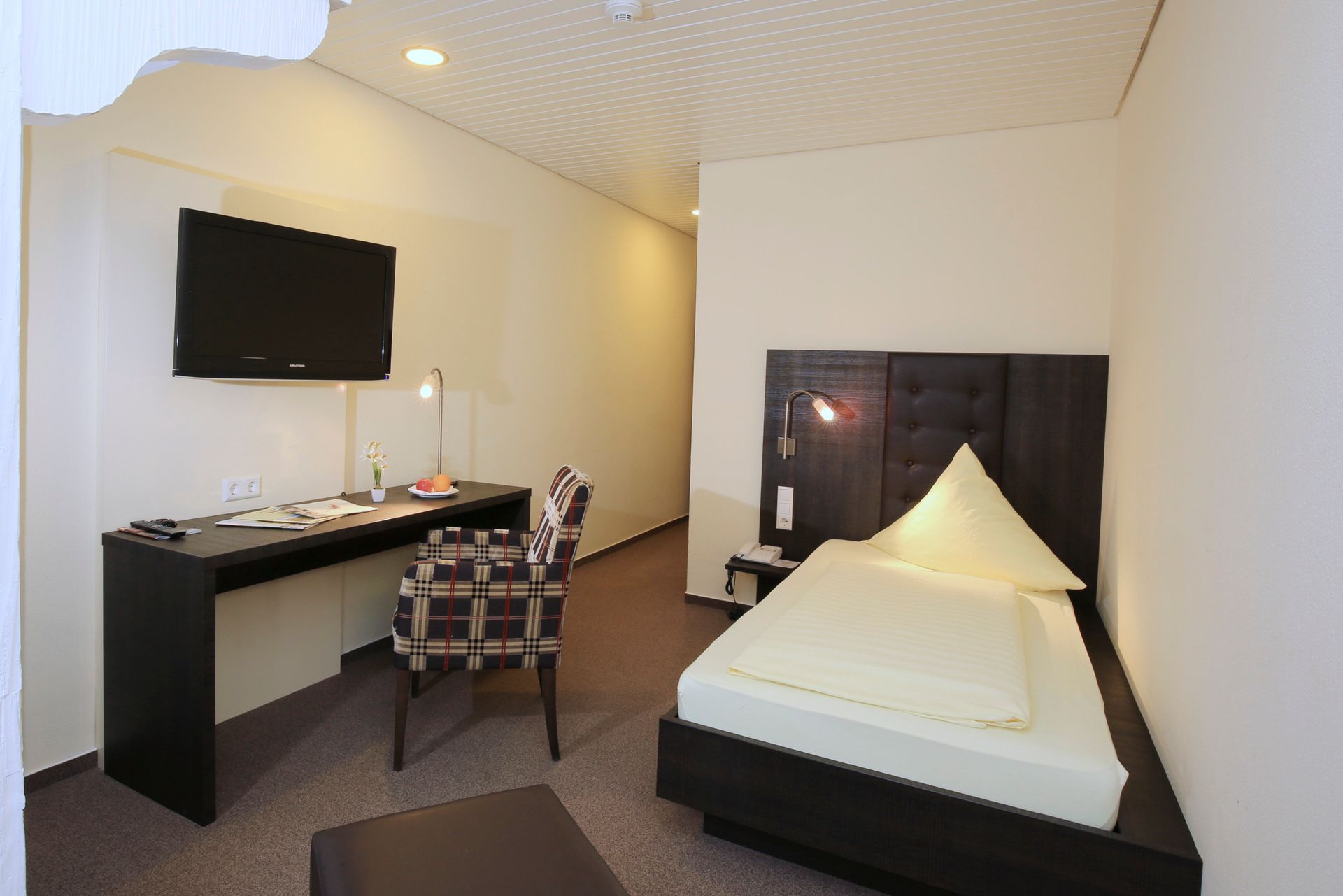 Ein Hotelzimmer mit Einzelbett, Schreibtisch, Stuhl und Fernseher.