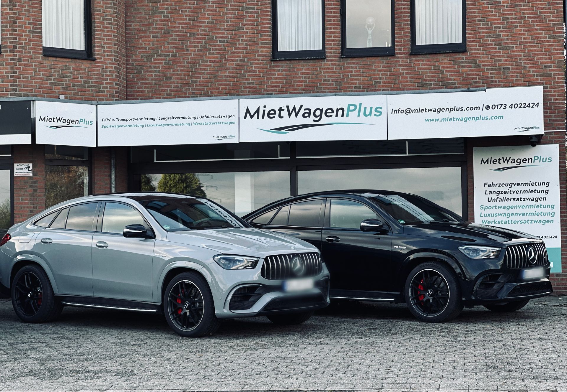 Frau in orangefarbenem Hemd telefoniert neben einem schwarzen Auto auf einem Parkplatz.