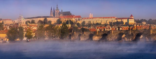 Sunrise cityscape with a cathedral above a foggy river and illuminated historic buildings