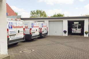 Weiße Servicewagen von Warmbold Id parken vor einer Garage. Ein Wagen steht in der offenen Garage.