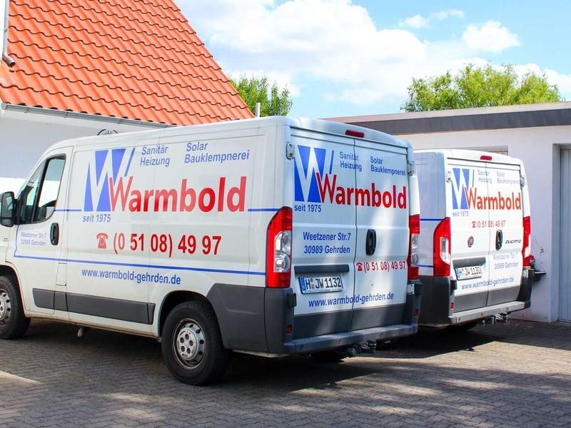 Drei weiße Lieferwagen mit dem „Warmbold“-Logo und Kontaktinformationen parken vor dem Gebäude.