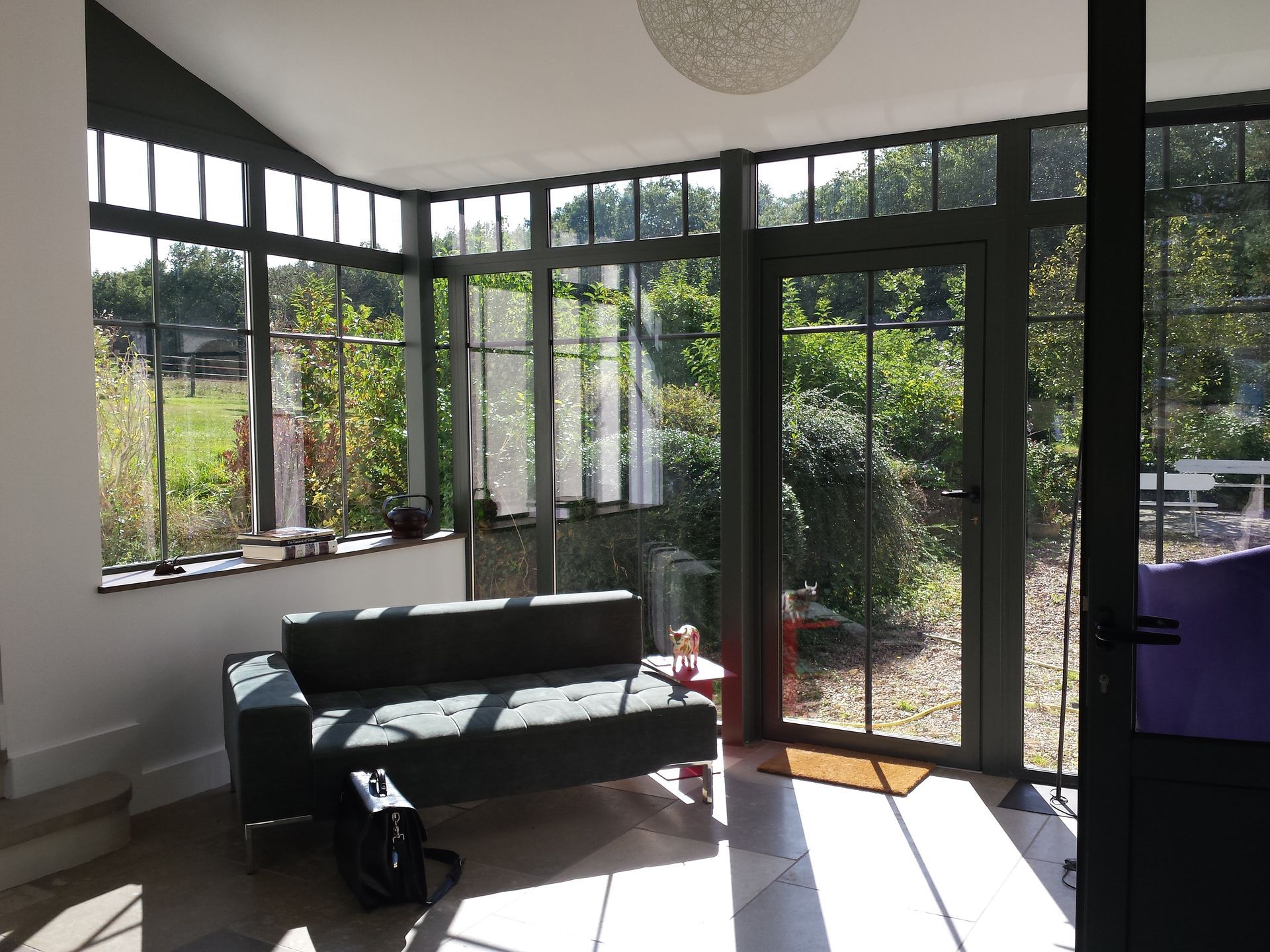 Canapé installé près d'une porte vitrée et baigné par la lumière d'une baie vitrée dans une extension de maison