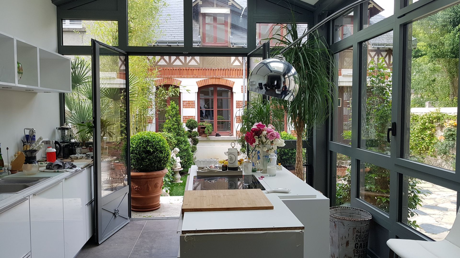 Cuisine dans une extension de maison entourée de baies vitrées qui donnent sur le jardin fleuri
