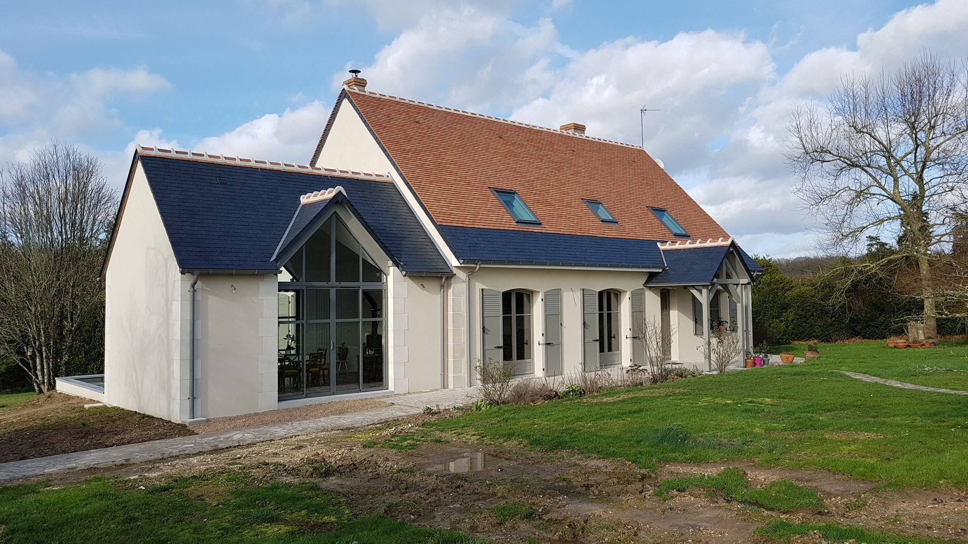 Extension de maison ajoutée à gauche d'une maison avec toiture bleue et grande verrière