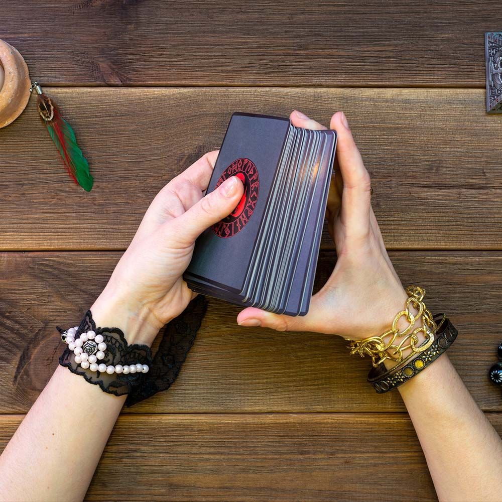 Una mujer sostiene una carta del tarot en sus manos sobre una mesa de madera.
