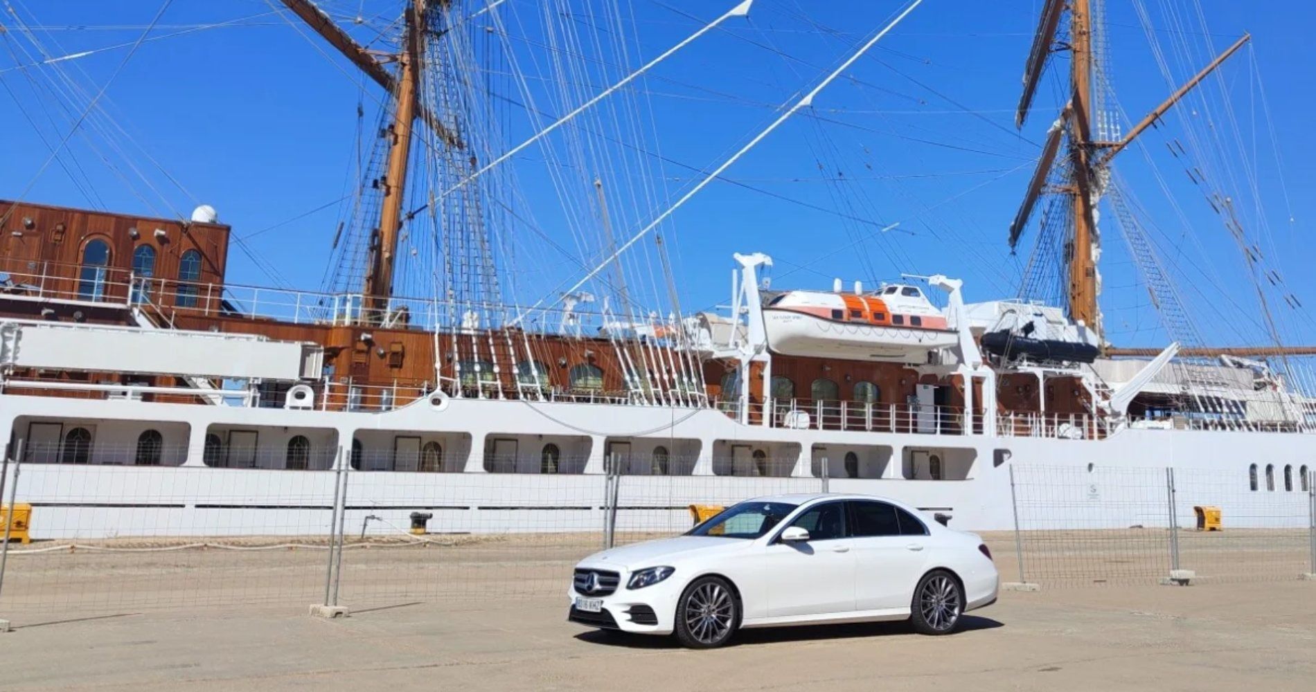 Un coche blanco está aparcado delante de un gran barco blanco.