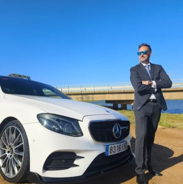 Un hombre con traje está parado frente a un Mercedes blanco.