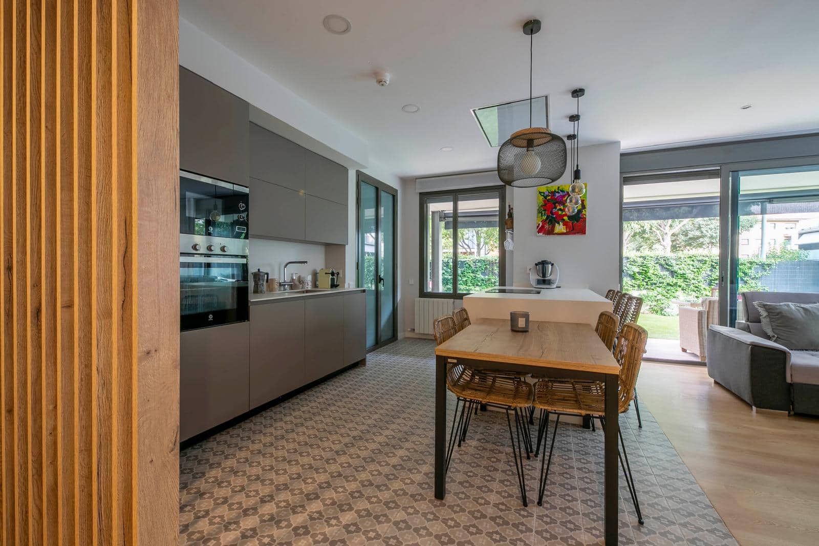 Cocina moderna y comedor con gabinetes grises, mesa de madera y acceso al exterior.