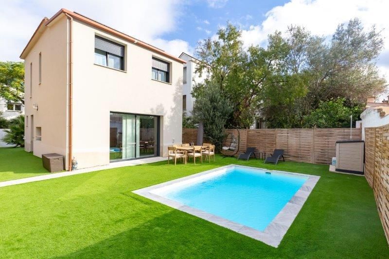 Patio trasero con piscina cuadrada, casa, césped verde y muebles de patio.