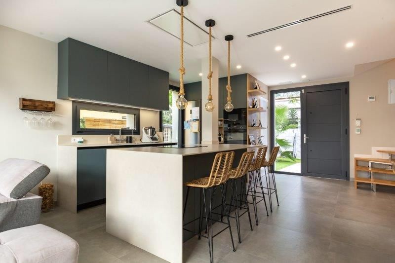 Cocina moderna con isla, asientos, gabinetes oscuros y piso de concreto.