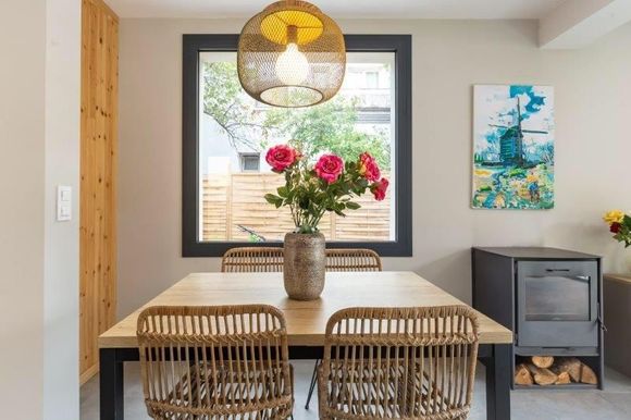 Comedor con mesa de madera, sillas de ratán y un jarrón de rosas rosas.