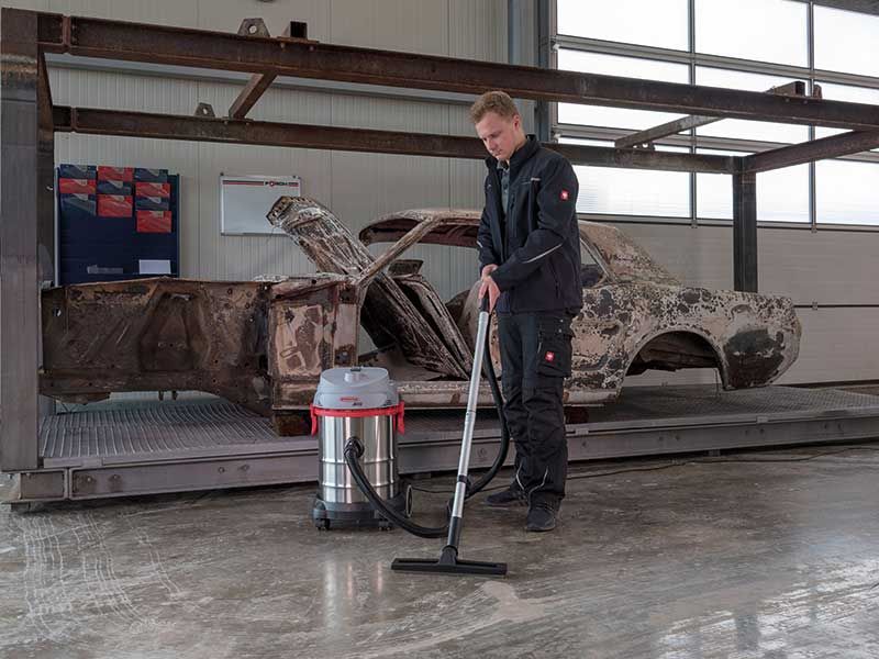 Ein Mann reinigt in einer Garage den Boden mit einem Staubsauger.