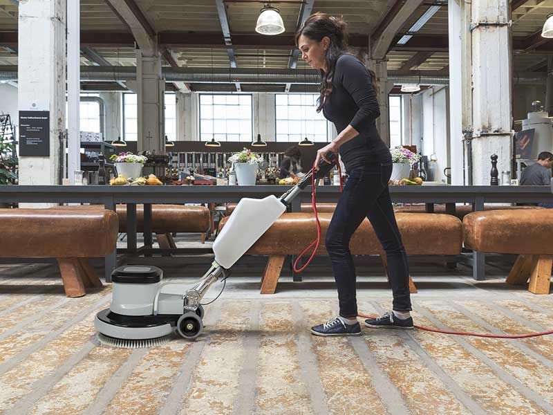 Eine Frau reinigt den Boden mit einer Maschine.