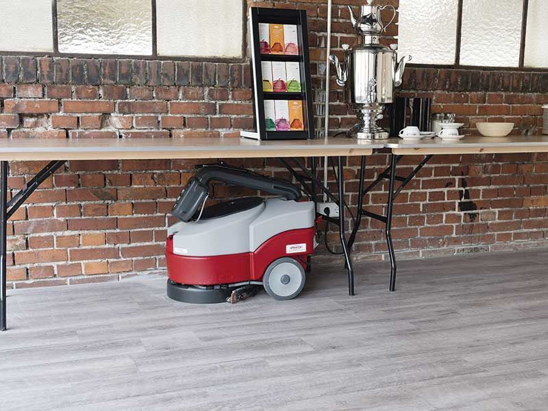 Eine rot-graue Maschine steht auf dem Boden vor einer Backsteinmauer