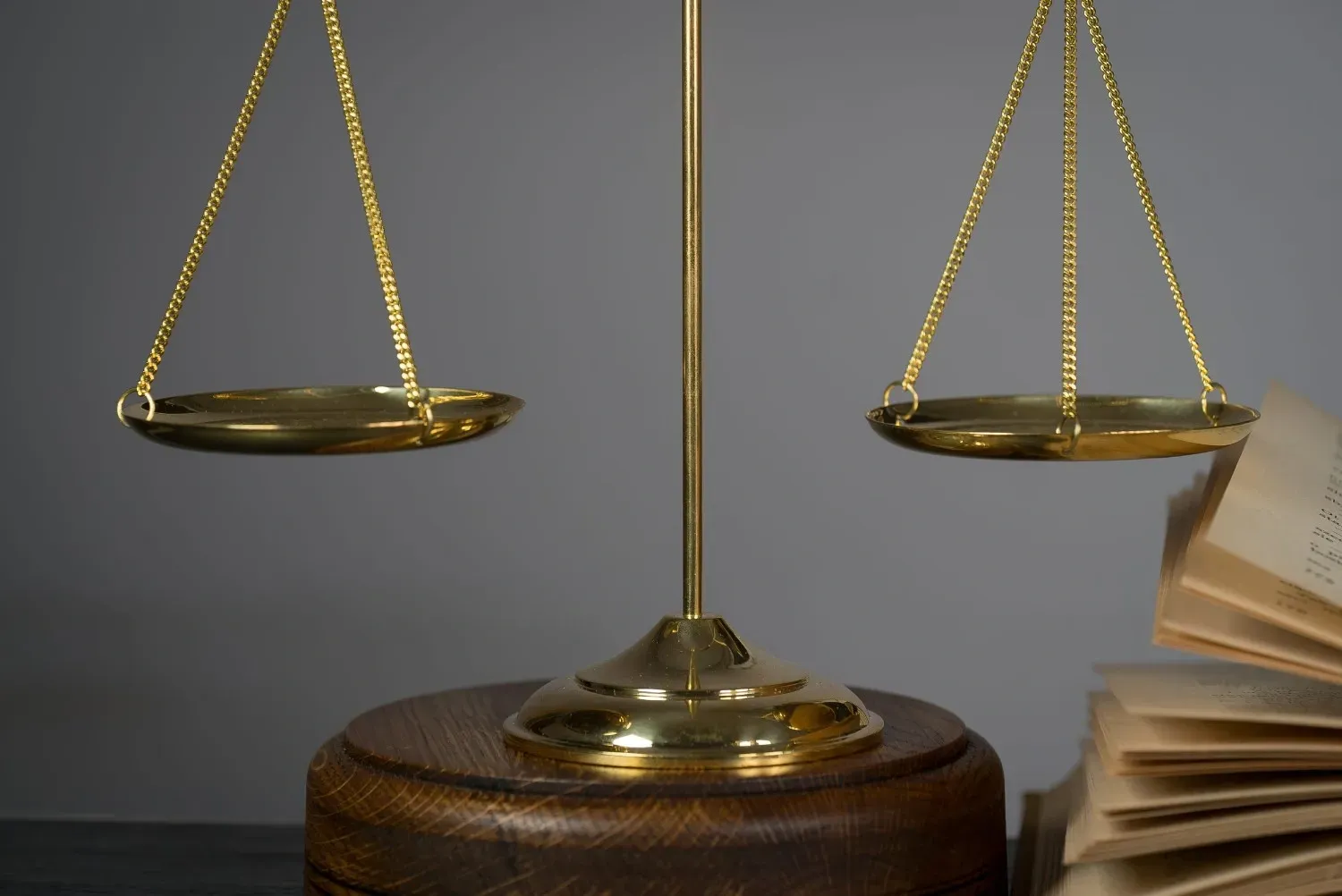 Una balanza de latón descansa sobre una base de madera junto a un libro abierto sobre un fondo gris.