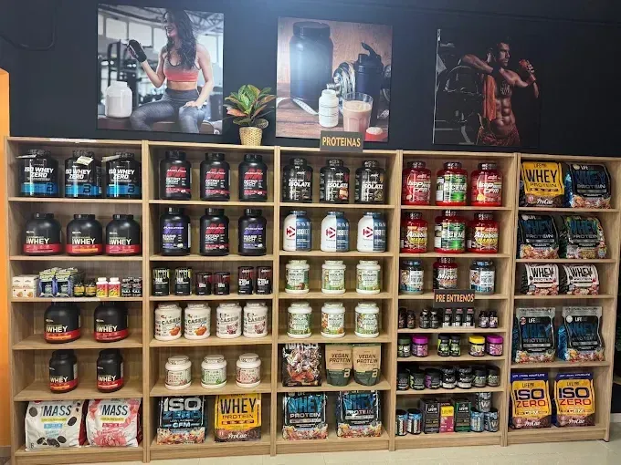 Estantes que muestran diversos suplementos de proteína en polvo en una tienda, con carteles promocionales encima.
