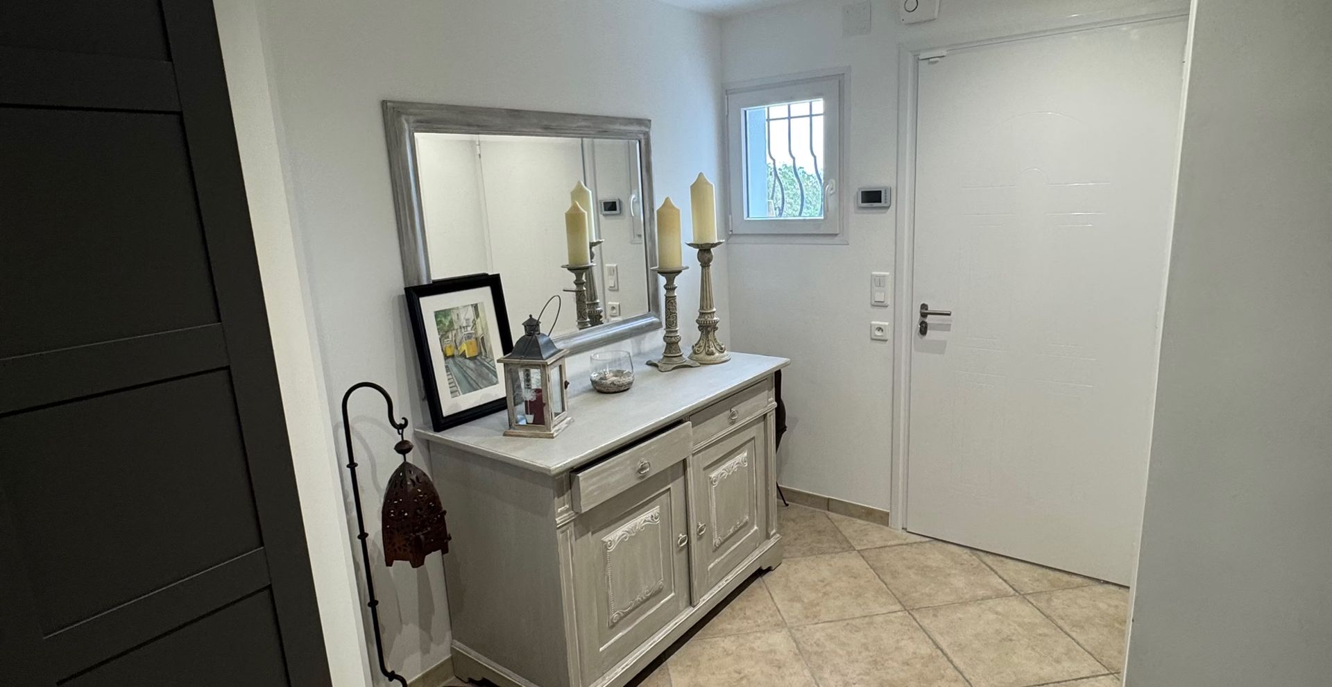 Couloir lumineux avec meuble-lavabo gris, miroir et porte blanche sur un sol carrelé beige.