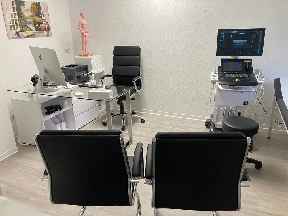 Eine Arztpraxis mit zwei Stühlen, einem Schreibtisch und einem Computer.