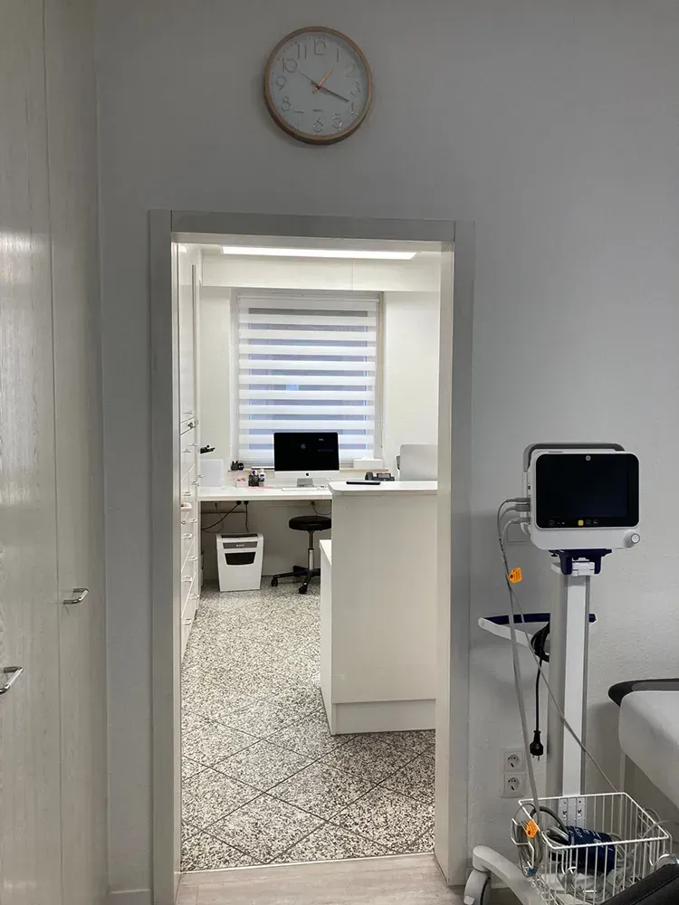 Eine Arztpraxis mit einer Uhr an der Wand und einem Monitor auf dem Boden.