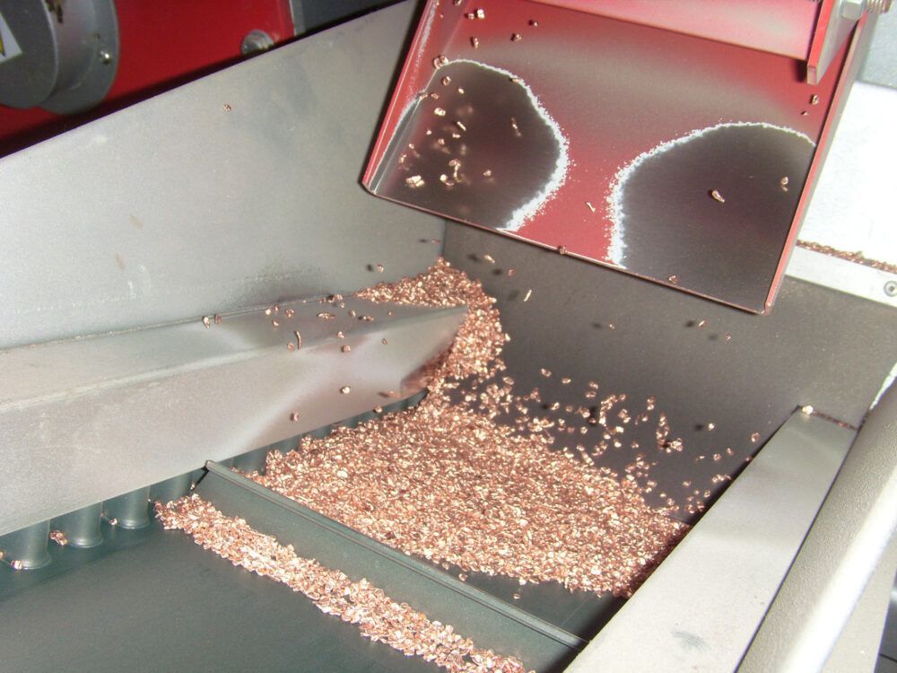 Des fragments de cuivre se déversent d'une goulotte métallique sur un tapis roulant.