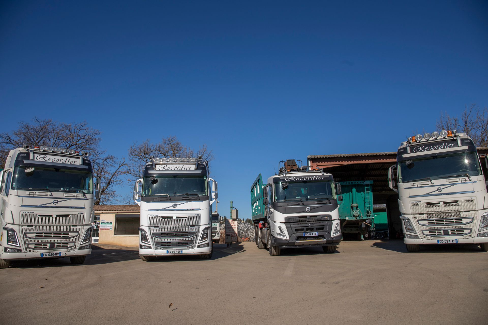 Quatre camions blancs garés devant un bâtiment sous un ciel bleu azur.