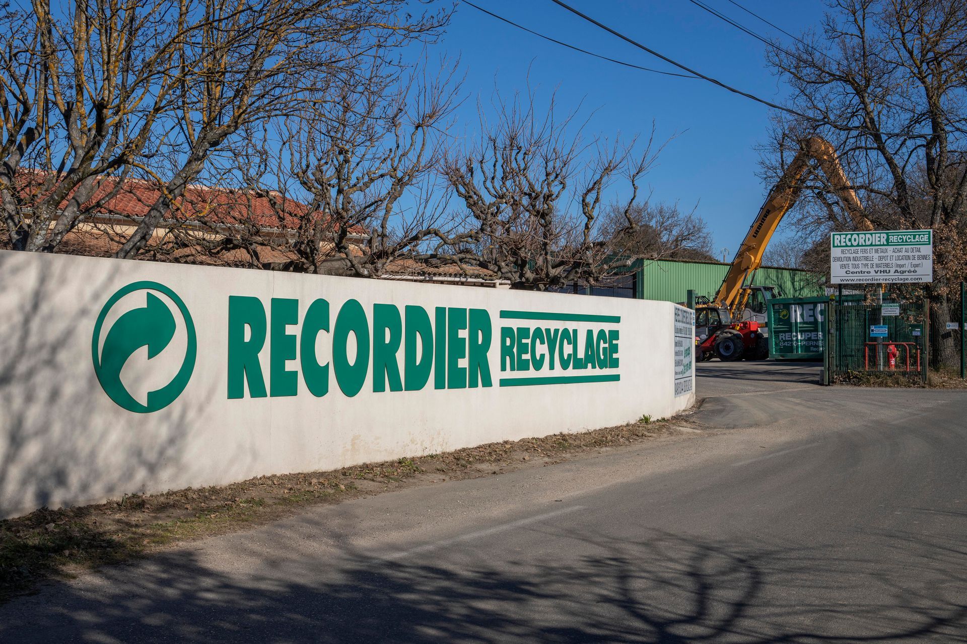 Mur blanc avec panneau vert « RECORDIER RECYCLAGE » et symbole de recyclage. Entrée d'un centre de recyclage.