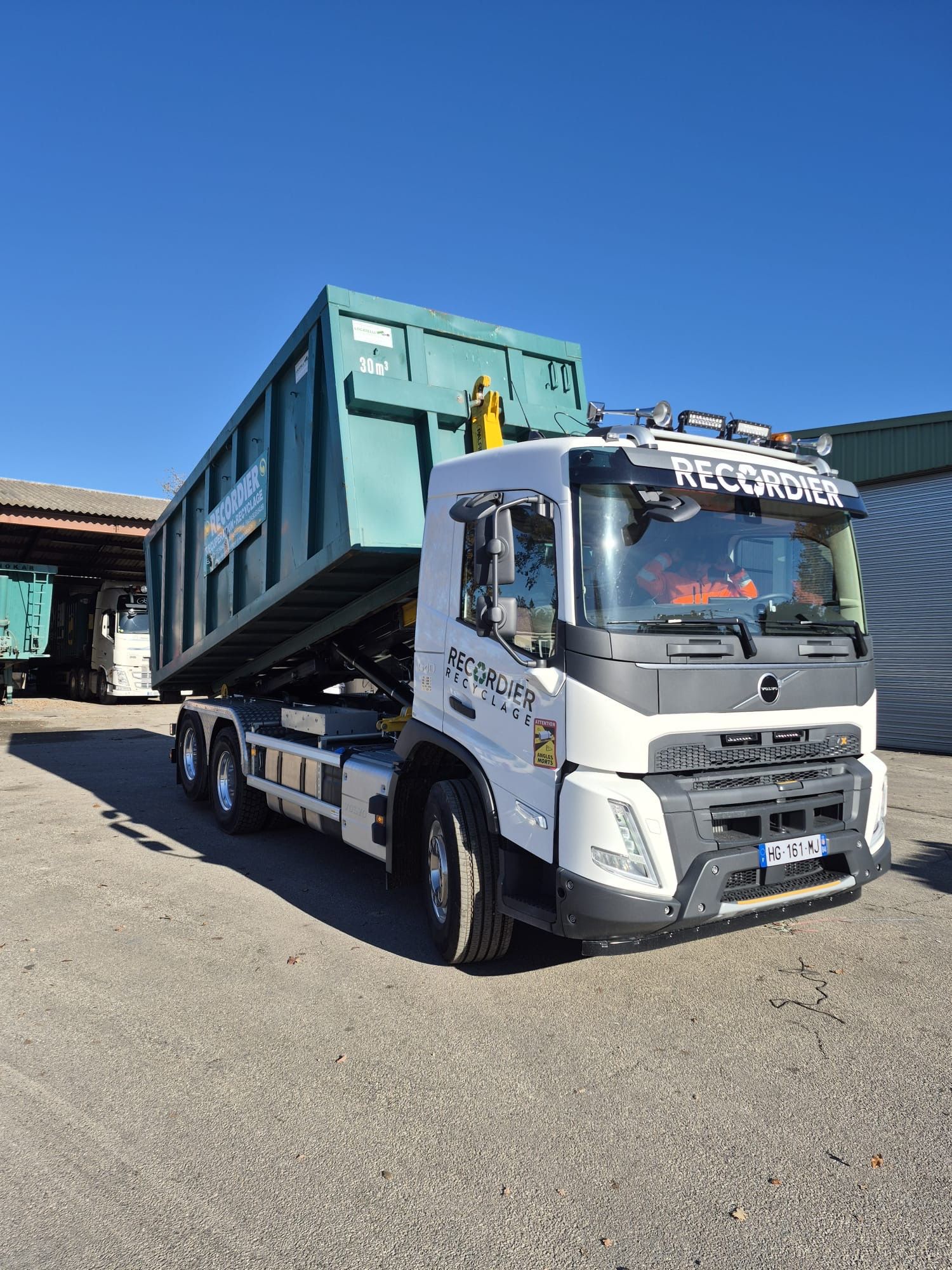 Camion-benne blanc avec conteneur vert en plein jour.