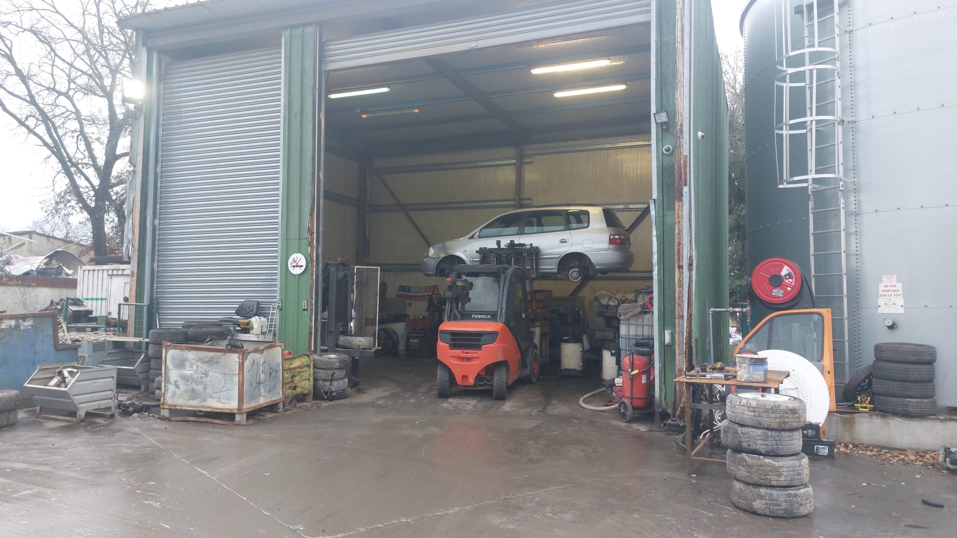Dans un garage, un chariot élévateur transporte deux voitures fortement endommagées ; un ouvrier se tient à proximité.