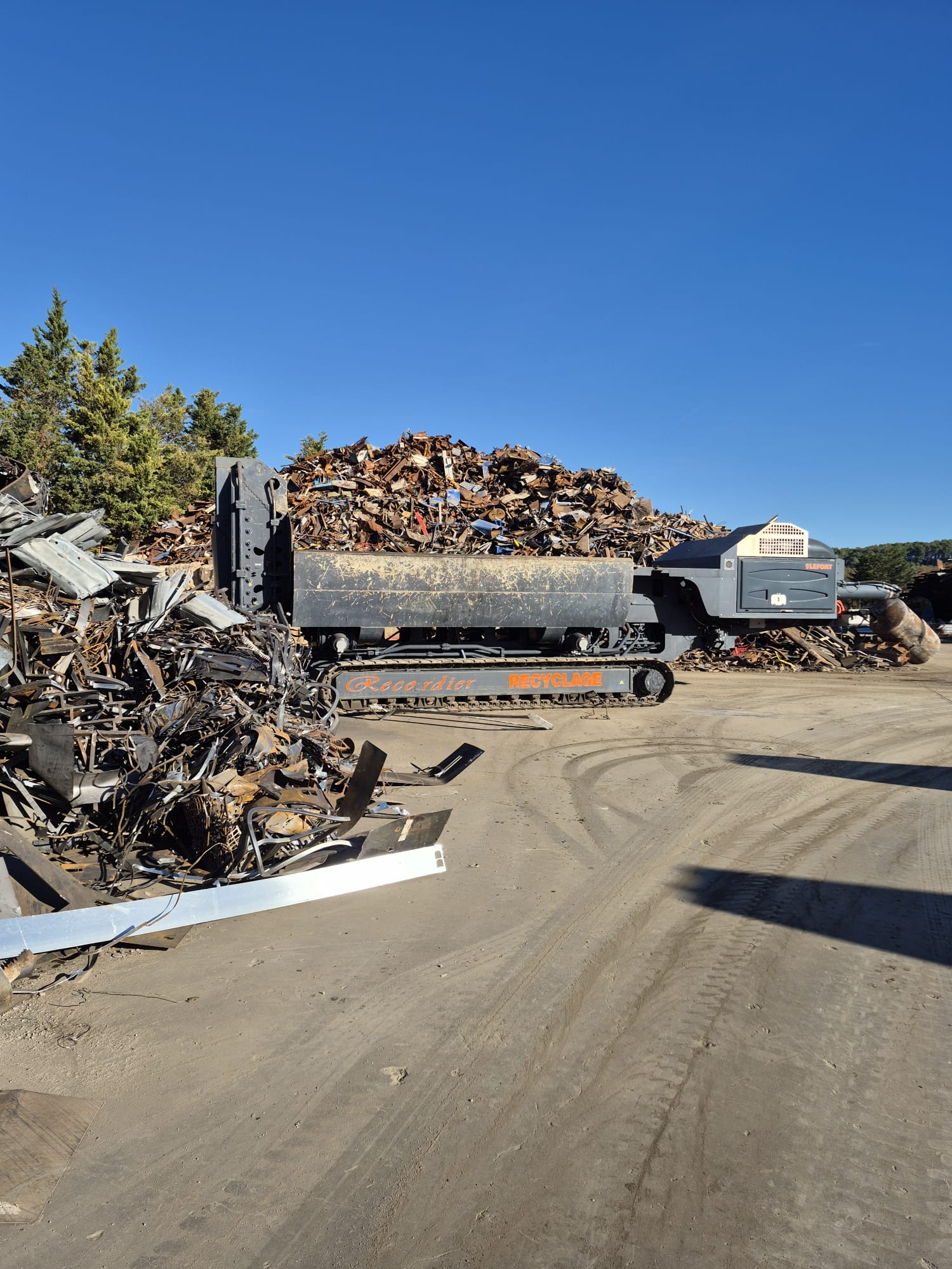 Centre de recyclage des métaux avec d'immenses tas de ferraille et une machine chenillée. Ciel bleu.